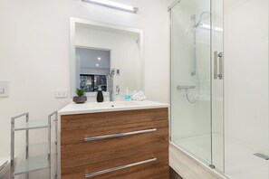 Ein modernes Badezimmer mit einem Holzbadezimmer-Möbel, einer Glasdusche und einem großen Spiegel.