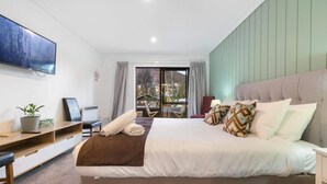 A hotel room with a bed, a desk, a TV, a plant, and a view of the outdoors. - Private Studio on Fryer (Queenstown)