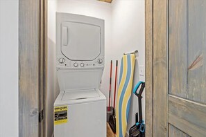A compact laundry room with a front-loading washing machine, a drying rack, and a broom. - "The Ridgeline" Modern Dog-Friendly Cabin Near PF & Gatlinburg (Sevierville)