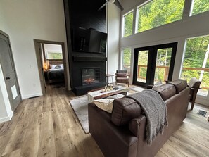Un moderno salón con chimenea, sofá de cuero y ventanas amplias con vistas al exterior.