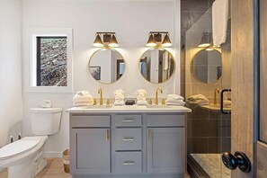 Une salle de bain moderne dotée d’un meuble-lavabo à deux vasques, de deux miroirs fixés au mur et d’un espace douche.
