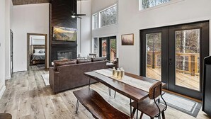 A spacious living area with a large wooden dining table, a sofa, and a fireplace. - "The Ridgeline" Modern Dog-Friendly Cabin Near PF & Gatlinburg (Sevierville)