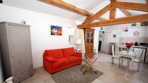 Een woonkamer met een rode bank, een kast, een schilderij en een keukenhoek met een tafel en stoelen.