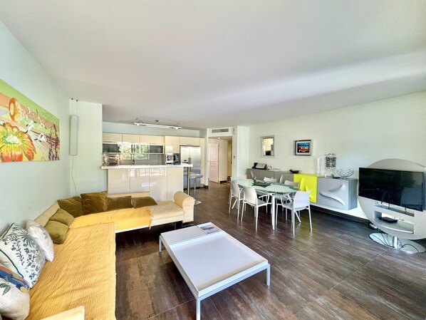 A modern living space with a sofa, coffee table, dining area, kitchen, and TV.