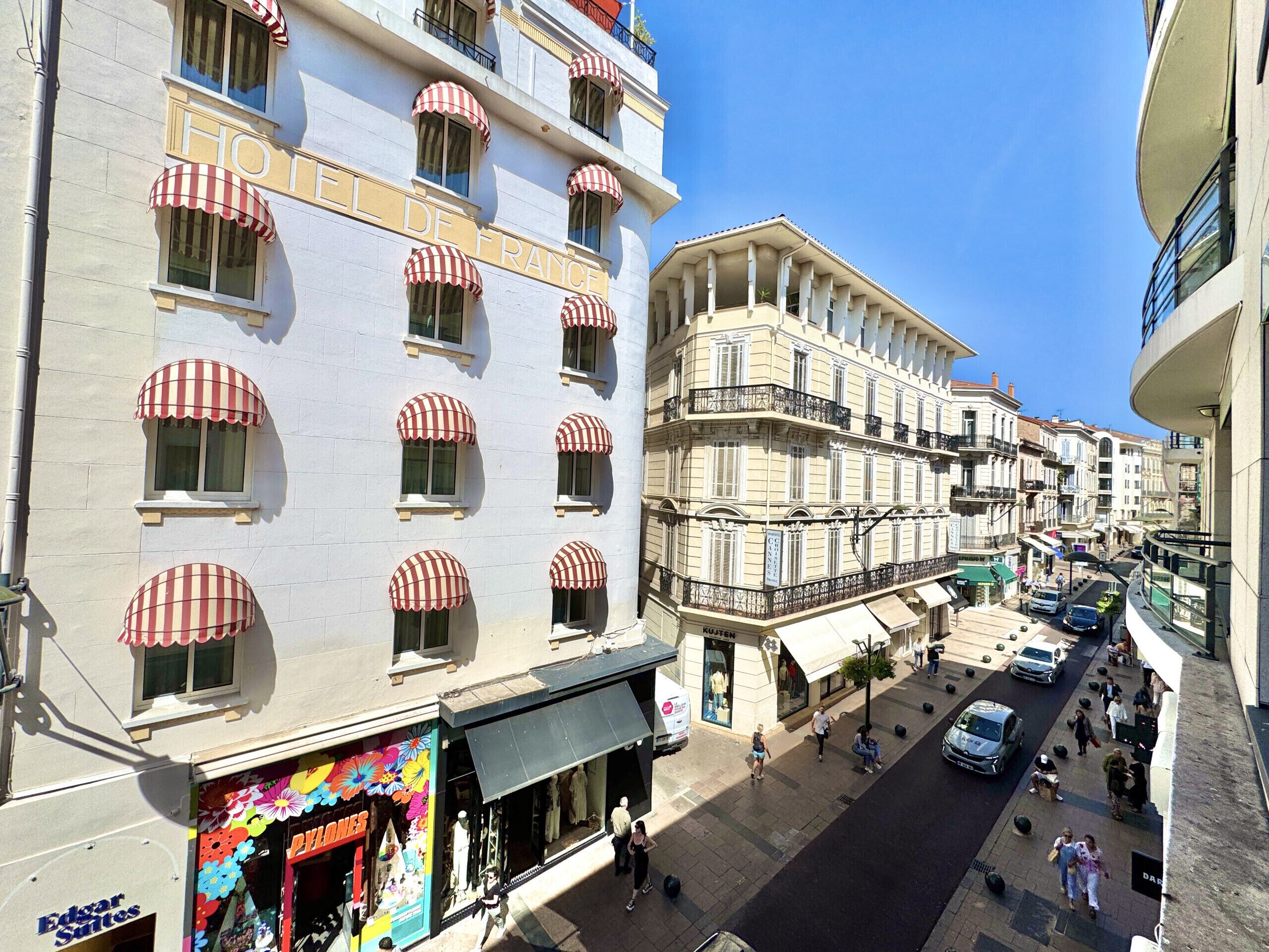 A hotel with multiple floors, red and white striped awnings over windows, and a street below with pedestrians and cars.