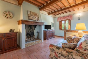 A living room with a fireplace, wooden beams, a television, and a floral sofa.