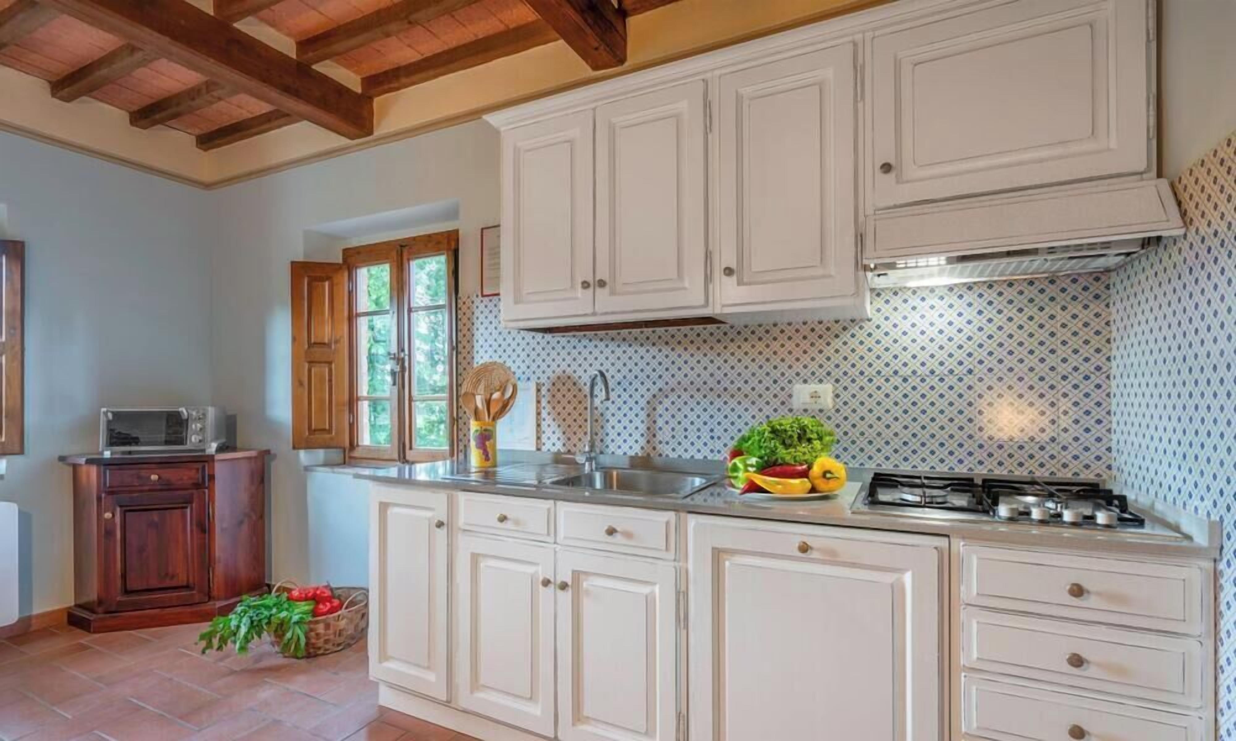 Una cocina con armarios blancos, una estufa y una ventana con persianas de madera.
