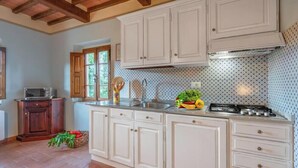 A kitchen with white cabinets, a stove, and a window with wooden shutters. - PINUS - First floor apartment 95 m2 (Montaione)