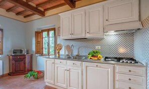 A kitchen with white cabinets, a stove, and a window with wooden shutters. - PINUS - First floor apartment 95 m2 (Montaione)