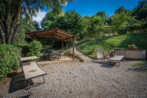 Een terras buiten met een pergola, zitplaatsen en een grindpad.
