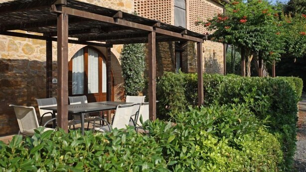 Un bâtiment en pierre doté d’une pergola, d’un espace extérieur aménagé pour s’asseoir et de haies bien entretenues.