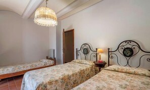 A room with two single beds, a chandelier, a wooden door, and a nightstand with a lamp. - JUNIPERUS - Ground floor apartment 95 m2 (Montaione)