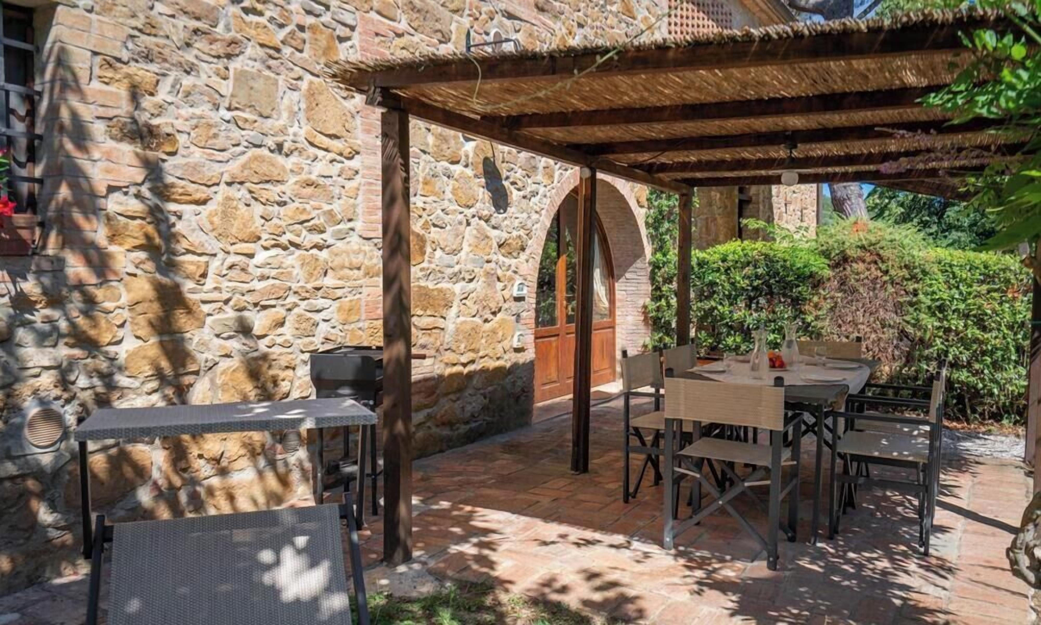 Une terrasse extérieure avec des murs en pierre, un espace salon abrité et une table dressée pour le repas.
