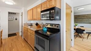 A modern kitchen with wooden cabinets, a stainless steel microwave, a black stove, and a teal kettle.