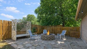 An outdoor patio with stone flooring, a fire pit, and two striped chairs.