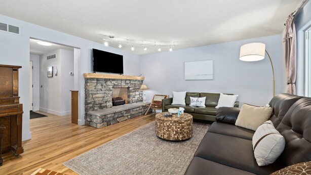 A living room with a stone fireplace, a leather sofa, a round coffee table, and a flat-screen TV mounted on the wall.