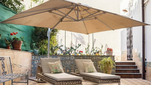 A patio with two lounge chairs, a large umbrella, and a tiled wall with potted plants. - Maridda sicilian vacation home (Giarre)