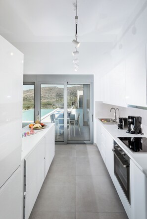 A modern kitchen with white cabinets, a built-in oven, and a view of a pool through glass doors. - Villa Klelia, a Newly Built 2023 Villa With Private Pool Next to Kissamos (Kissamos)