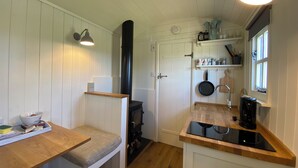 Una cocina compacta con paredes de madera blanca, estufa empotrada, banco de madera, encimera con cafetera y un colgador para ollas.