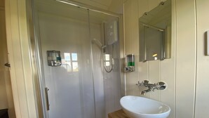 Un baño moderno con cabina de ducha de vidrio, un lavamanos blanco sobre encimera de madera y un espejo sobre el lavamanos.