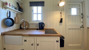 Una cocina con armarios blancos, encimera de madera, un lavabo, un hervidor y una ventana con persianas.