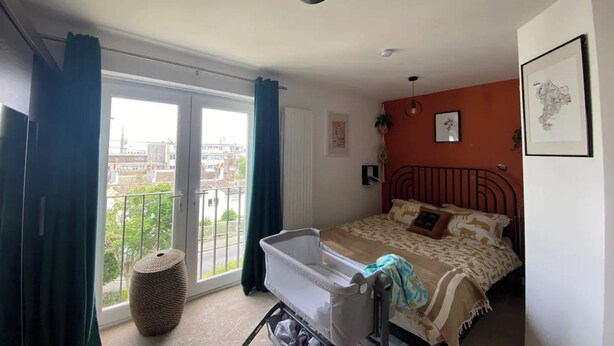 A bedroom with a bed, a crib, a window with curtains, and a balcony with a view. - Spacious & Central 2BD House - Brighton (Brighton)
