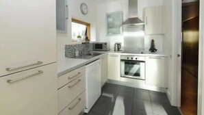 Una cocina compacta con gabinetes blancos, un microondas, un hervidor y una estufa.
