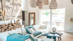 A modern living room with a white sofa, blue throw pillows, and a large window with a view of the outdoors. - Villa La Nîmoise (Nîmes)
