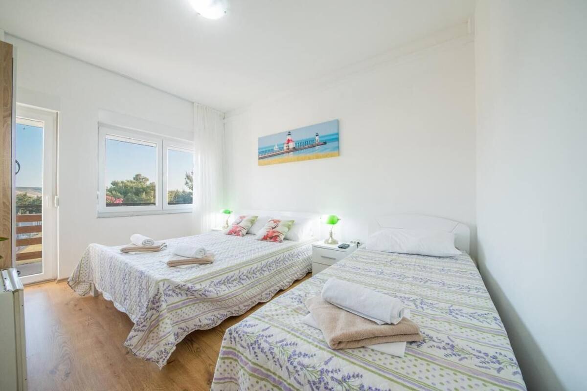 A bedroom with two beds, a painting of a lighthouse, and a balcony with a view.