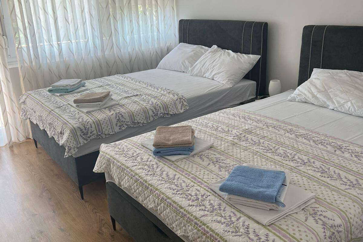 Two single beds with headboards, a wooden floor, and a window with sheer curtains.