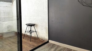 A room with a sliding glass door leading to an outdoor area, a small black grill table, and a geometric wall decoration. - Home for family or business stays (Cambrai)