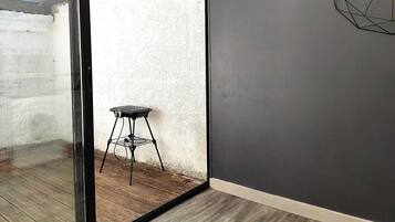 Une pièce dotée d’une porte-fenêtre coulissante donnant sur un espace extérieur, d’une petite table de barbecue noire et d’une décoration murale aux motifs géométriques.