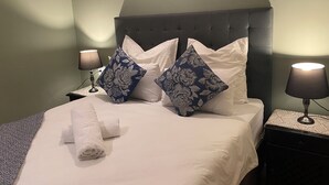A neatly made bed with white linens and blue floral pillows, two bedside lamps, and a folded towel on the bed.