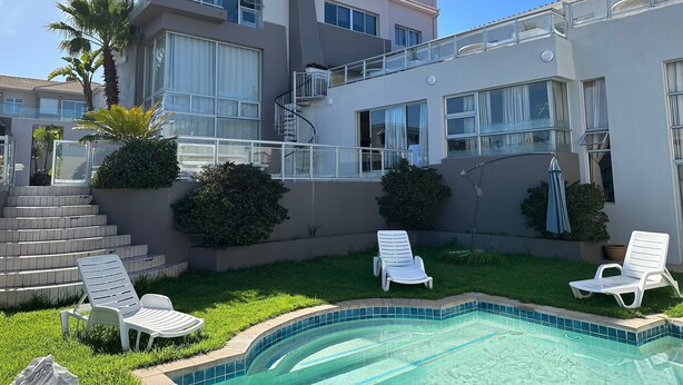 A modern two-story house with a swimming pool, outdoor seating, and a staircase leading to the upper floor.
