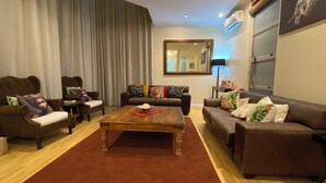 A living room with a brown sofa, two armchairs, a wooden coffee table, and a red rug.