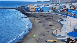 Eine Küstenstadt mit Strand, Gebäuden und Windkraftanlagen im Hintergrund.