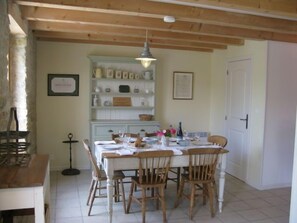Un coin repas avec une table en bois dressée pour quatre personnes, entourée de chaises en bois. Un buffet blanc aux portes vitrées est adossé au mur, et un certificat encadré y est accroché.