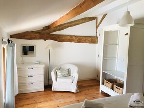 Une chambre avec un plafond en bois, une chaise blanche, une table de chevet, une lampe et une armoire.