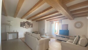 A living room with wooden beams, a sofa, a TV, and a dining area.