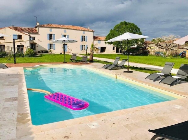 Une piscine rectangulaire avec un flotteur gonflable rose, entourée de chaises longues et de parasols, avec un bâtiment en arrière-plan.