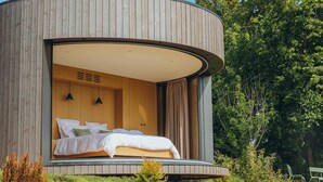 Una cabaña de madera moderna y circular con una cama grande y vistas al bosque circundante.