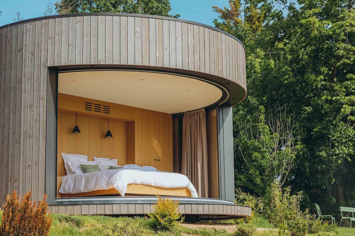 Une cabane moderne en bois, de forme circulaire, dotée d’un grand lit et offrant une vue sur la forêt environnante.