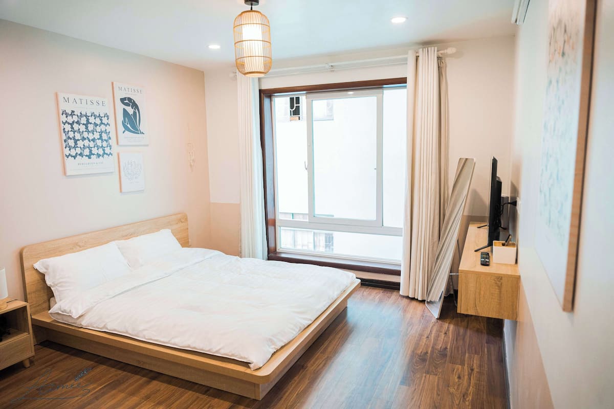 A bedroom with a wooden bed, a nightstand, a desk with a lamp, and a window with curtains.