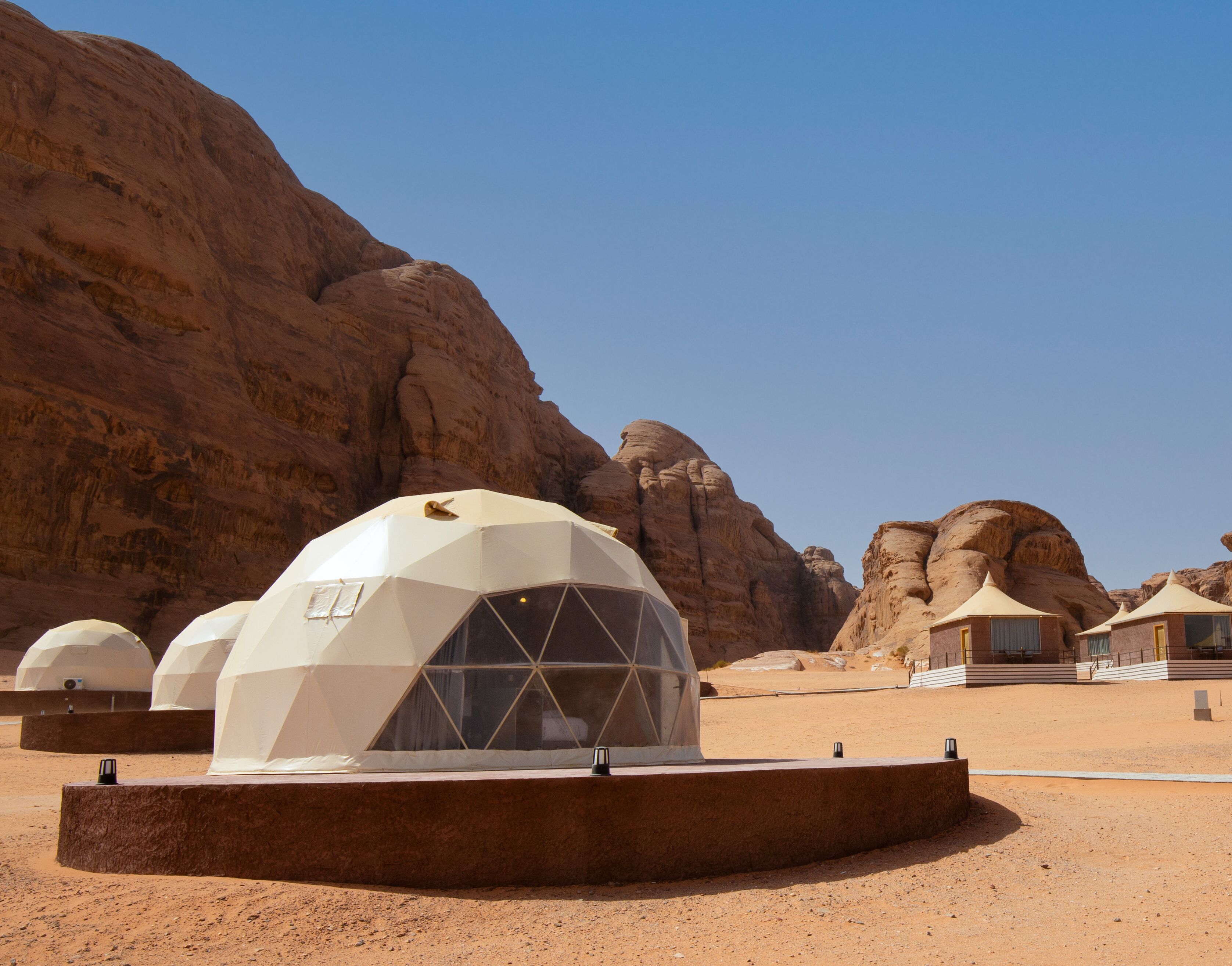 A desert landscape with multiple dome-shaped structures, likely accommodations, surrounded by rocky terrain and clear skies.