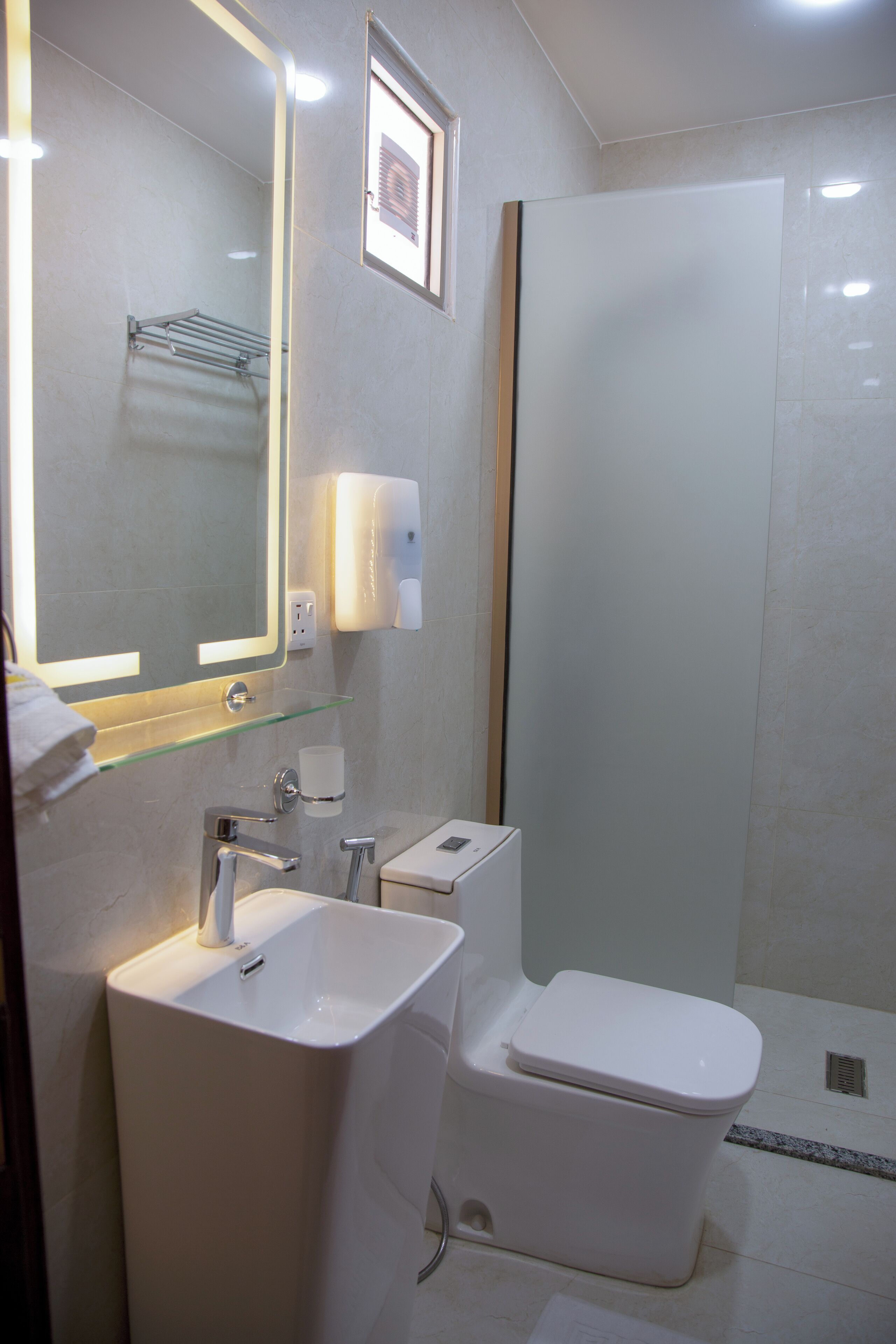 Une salle de bain moderne avec une étagère en verre, un lavabo blanc, des toilettes et une douche à parois de verre.