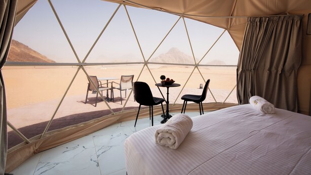 Een tent met een bed, twee stoelen, een klein tafeltje en uitzicht op een woestijnlandschap.