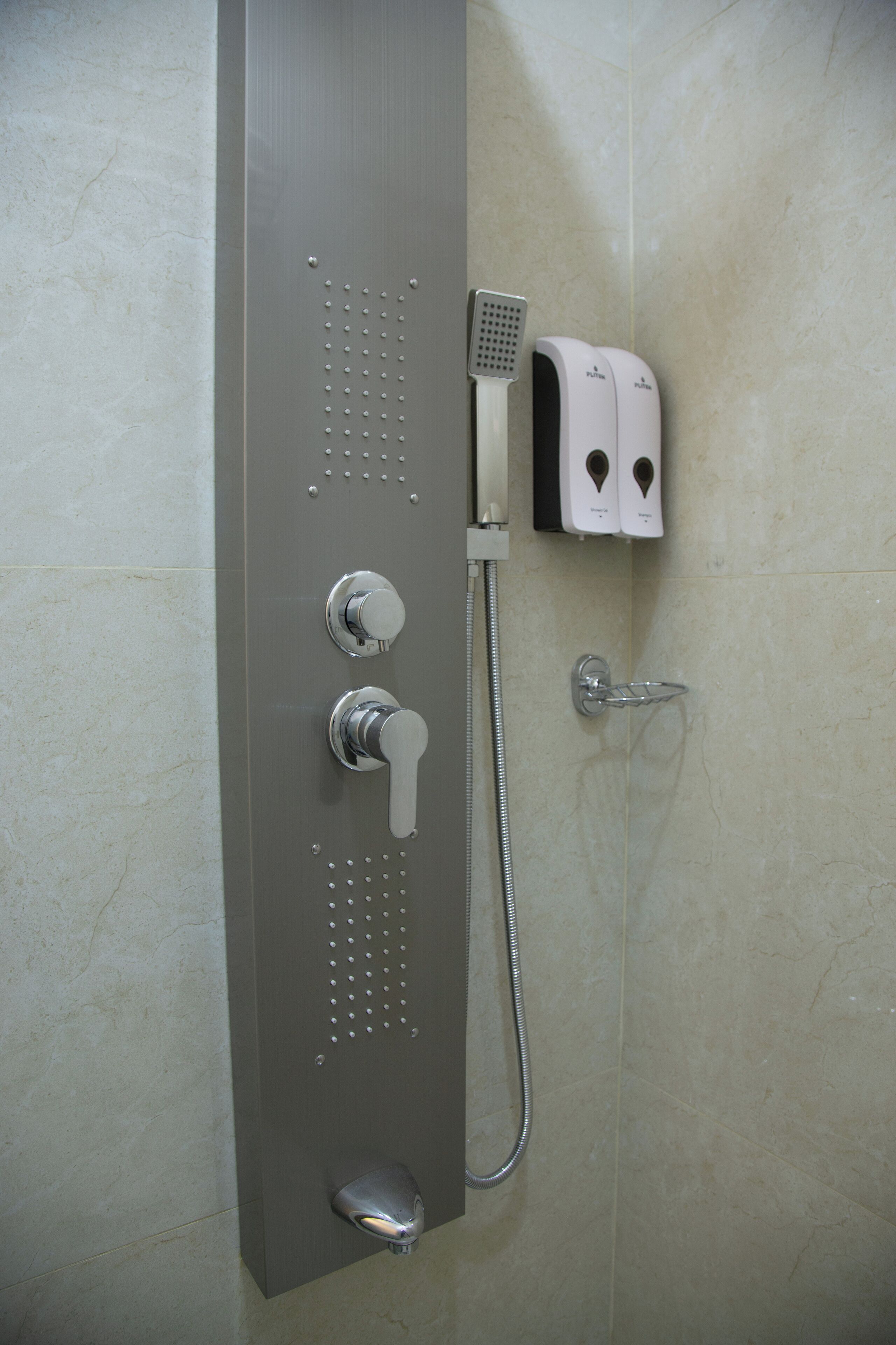 A shower with a handheld showerhead, a wall-mounted faucet, and a soap dispenser.