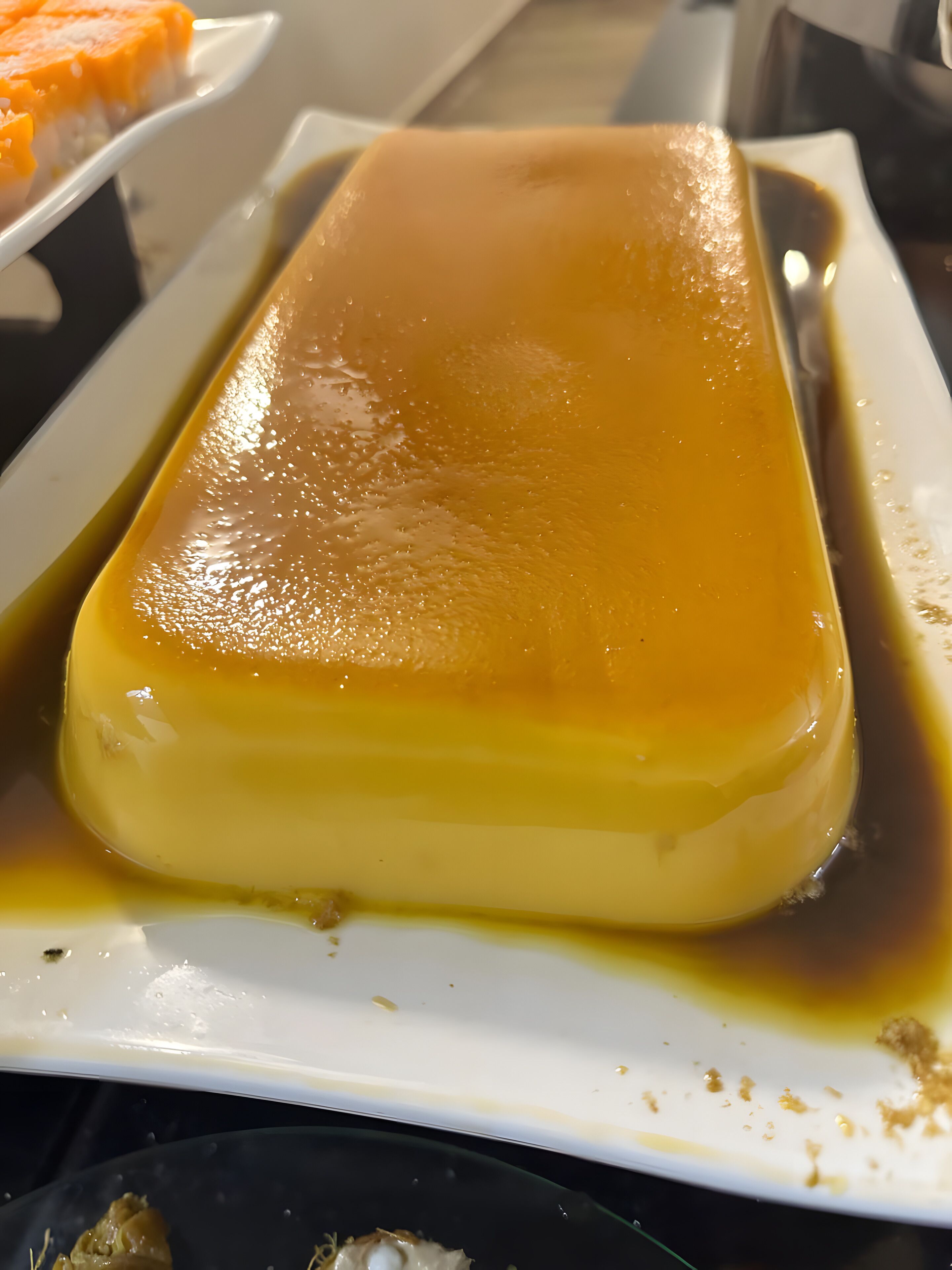 Un flan au caramel rectangulaire, servi sur une assiette blanche, avec une sauce au caramel qui l’entoure.