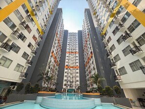 Un immeuble résidentiel de grande hauteur doté de nombreux balcons, d’une piscine centrale et entouré de verdure.