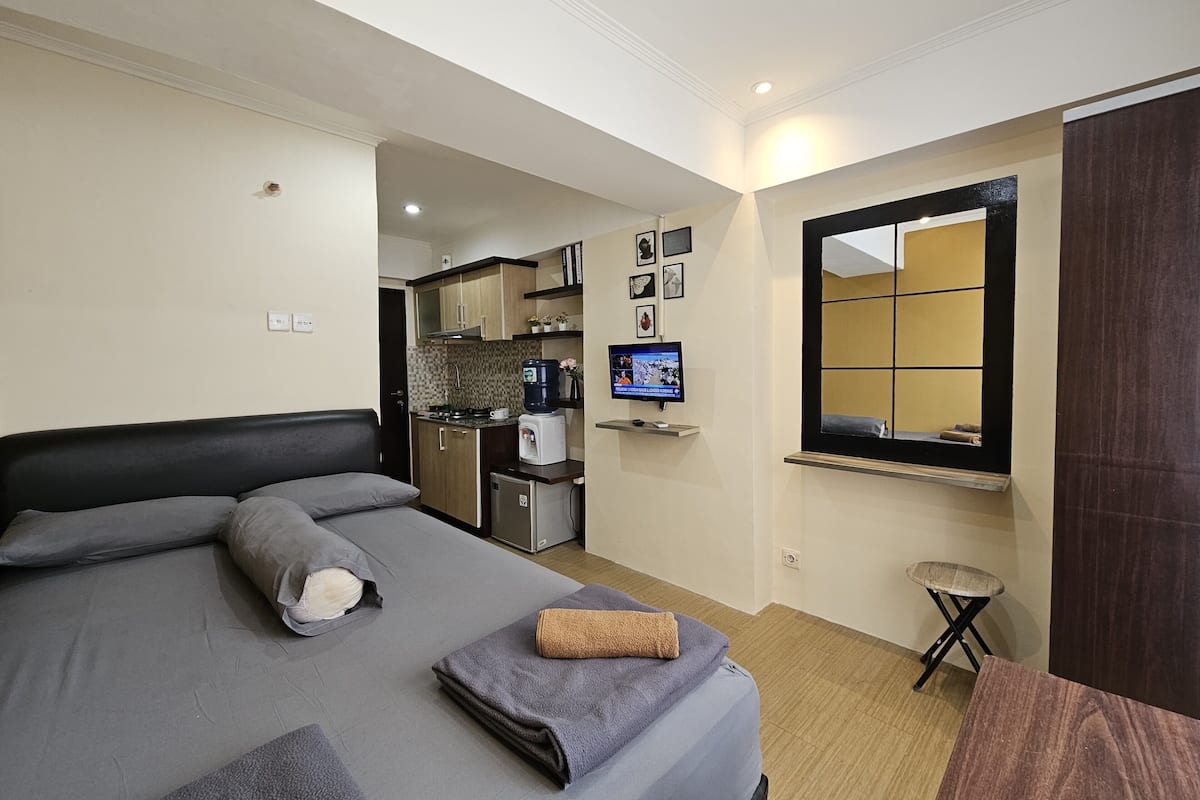 Une chambre d’hôtel compacte comprenant un lit, une petite kitchenette, une télévision et une fenêtre avec un miroir.
